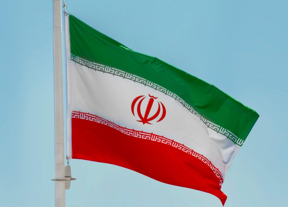 Low-angle view of the Iranian flag waving on a flagpole against a clear blue sky in Tehran, Iran.
