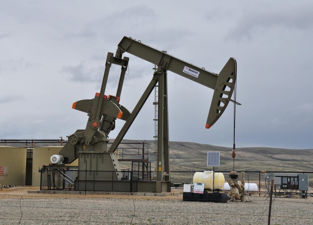 Oil pump jack and equipment at remote industrial site under cloudy sky.