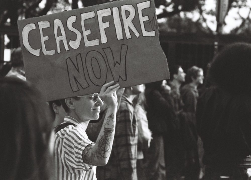 Black and white photo of a protest in Lisbon with a person holding a 'Ceasefire Now' sign.