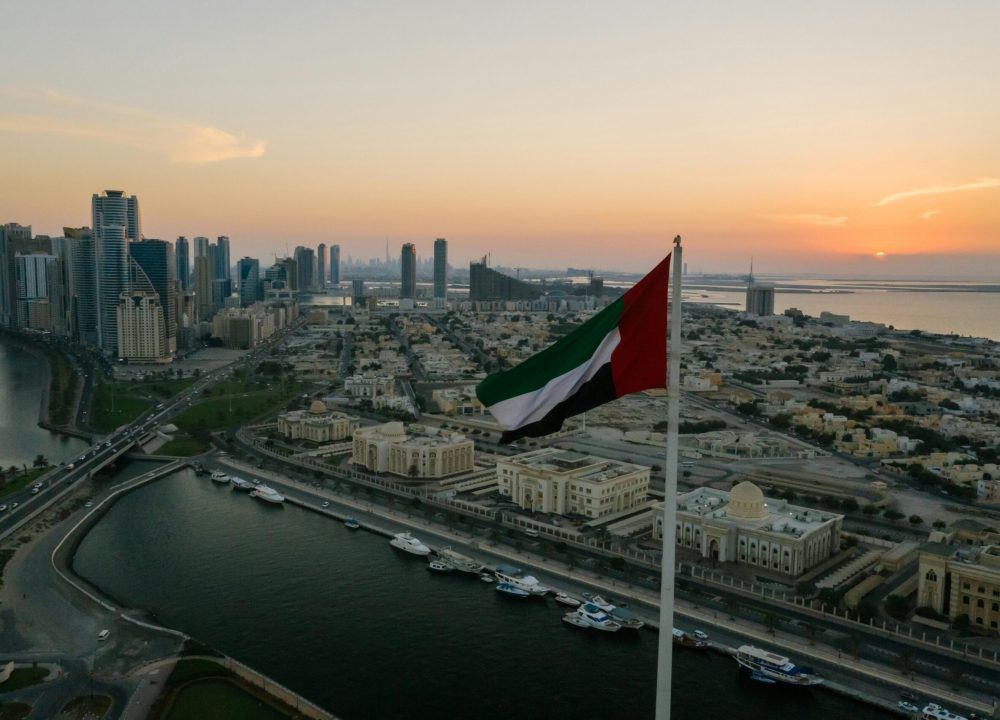 A breathtaking aerial view of a UAE city skyline with a prominent national flag at sunset, showcasing urban architecture.